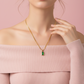Woman wearing a gold necklace with a green gemstone pendant against a pink background