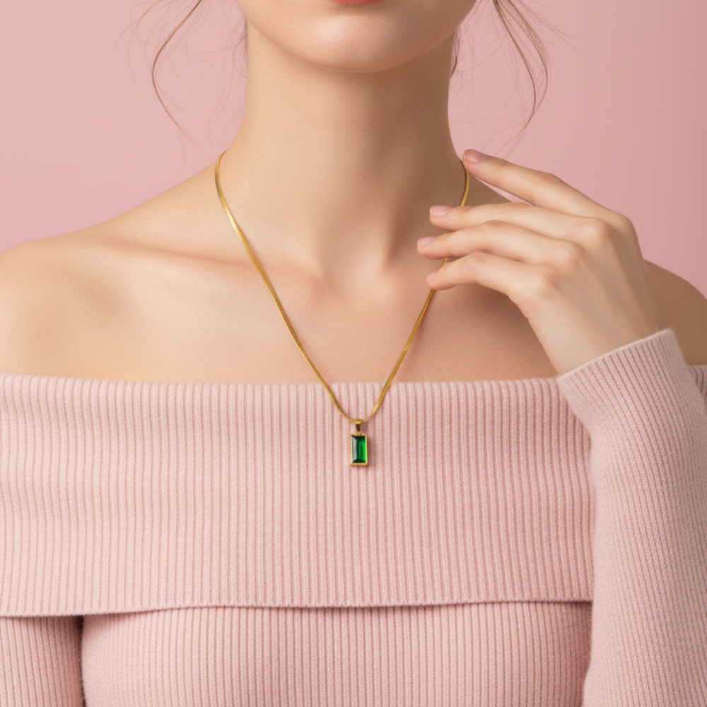 Woman wearing a gold necklace with a green gemstone pendant against a pink background