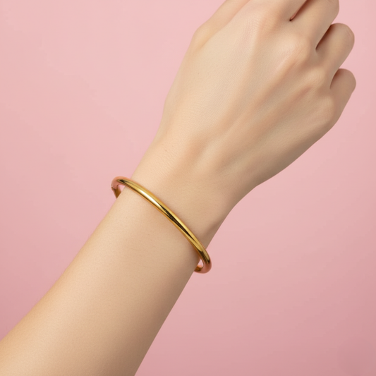 Gold bracelet on a wrist against a pink background