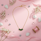 Gold necklace with green gemstones on a pink background with flowers and pearls