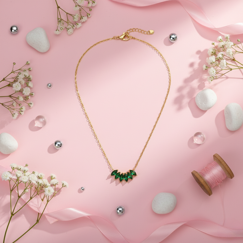 Gold necklace with green gemstones on a pink background with flowers and pearls
