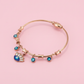 Rose gold bracelet with evil eye charms on a pink background