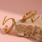 Gold open rings with embedded stones on a stone surface with a pink background