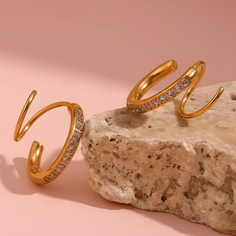 Gold open rings with embedded stones on a stone surface with a pink background