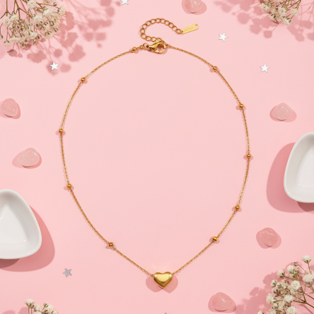 Gold necklace with a heart pendant on a pink background with flowers and heart-shaped objects.